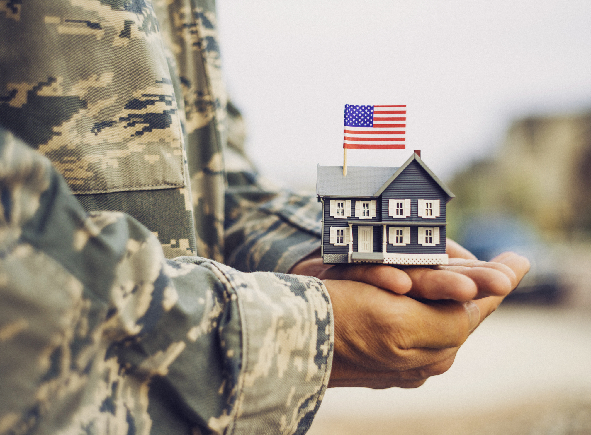 Servicemember holding a small wooden house model with an American Flag on it.