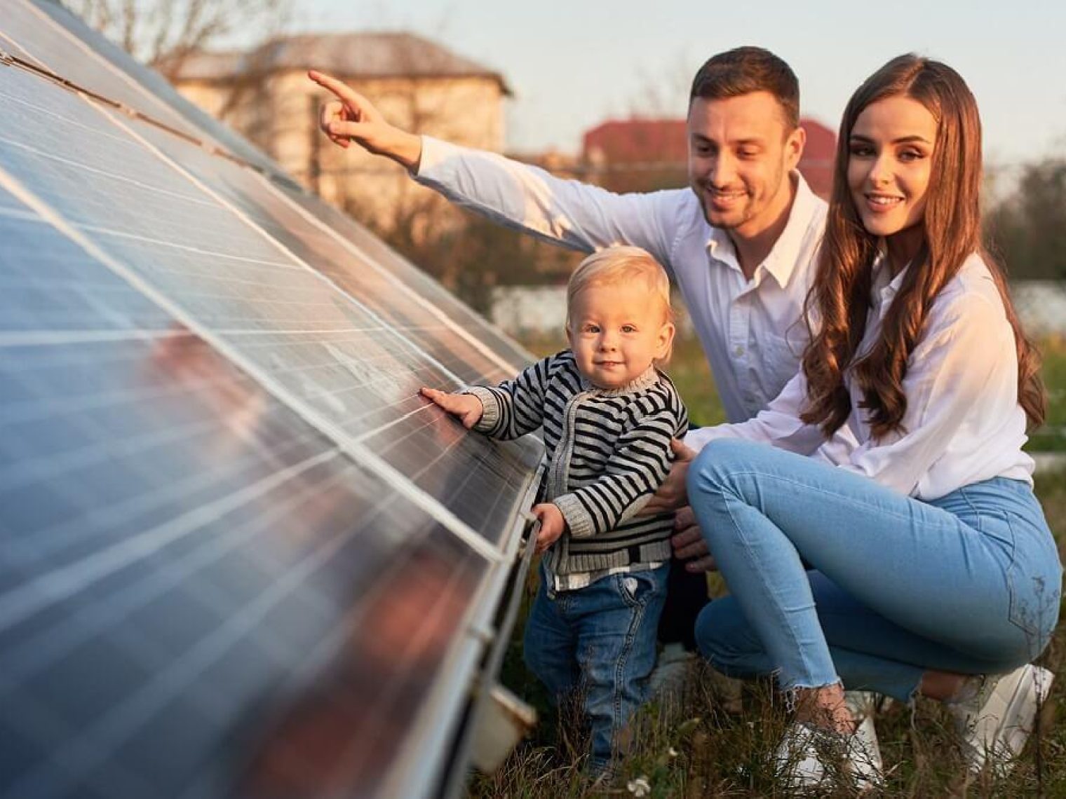 Family of three squatting next to a solar panel.