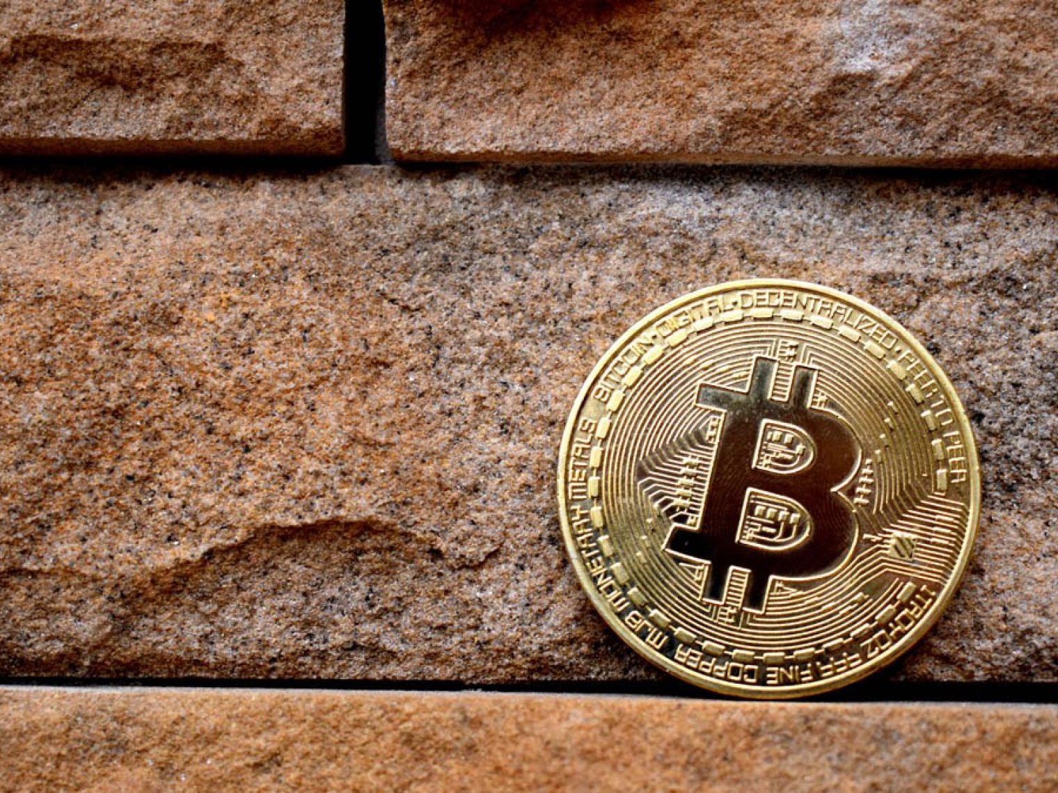 Physical bitcoin leans on a brick wall.