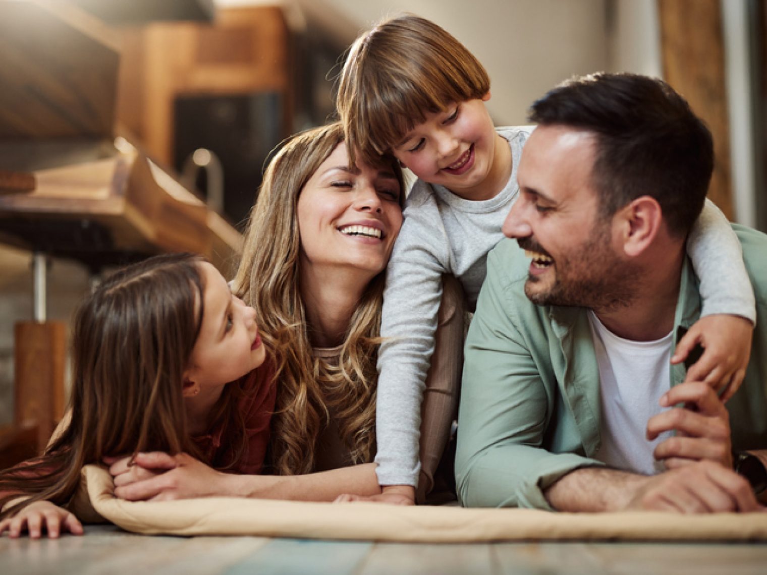 A happy family moment with a mother, father, and two children snuggling and laughing together in a cozy, indoor setting.