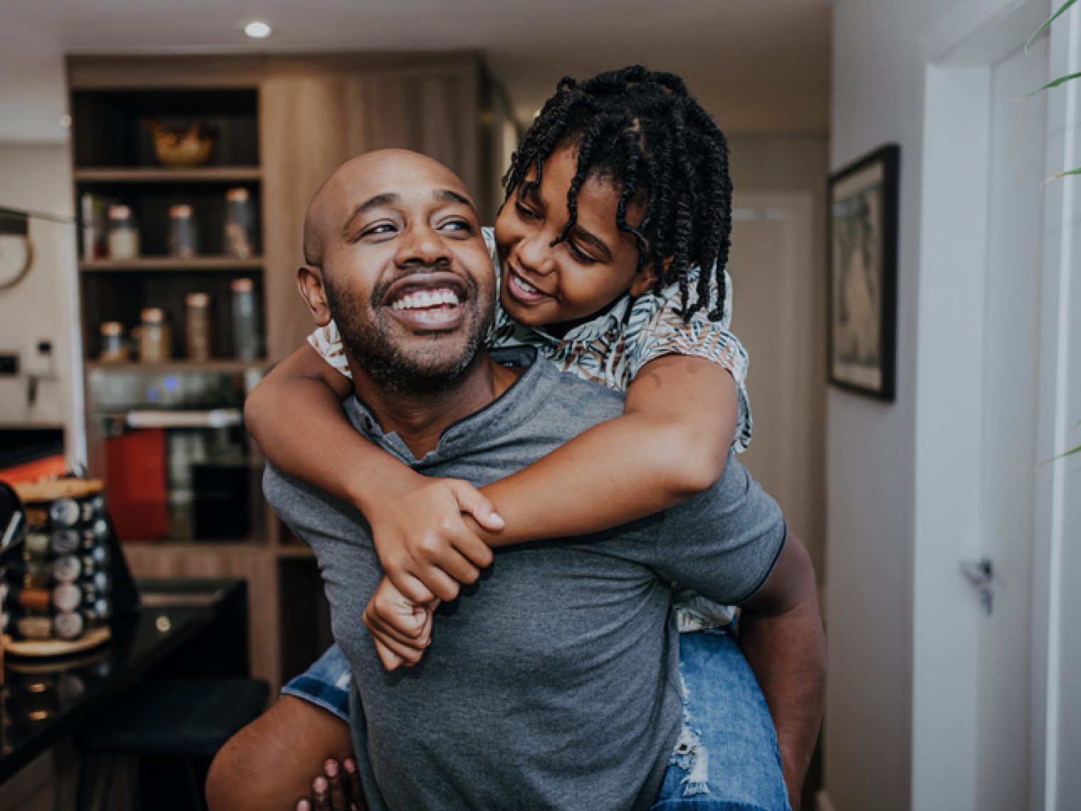 A joyful moment as a father and daughter share a loving embrace, with the child riding piggyback, both smiling in a cozy home setting.