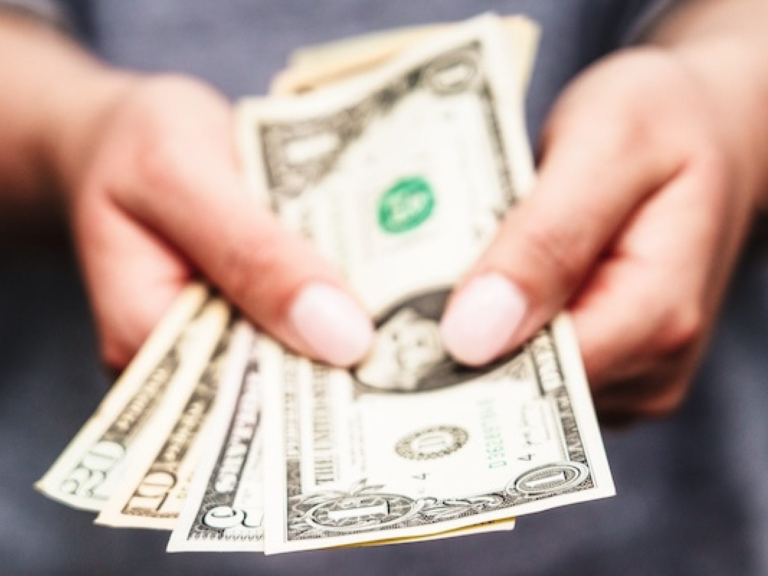 Close up of hands holding out US dollar bills.