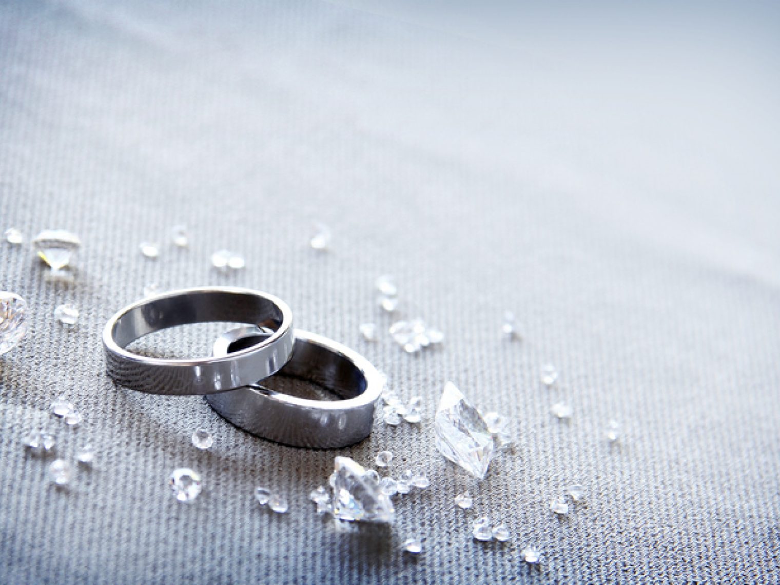 Two wedding bands lie amidst scattered crystals on a textured fabric.