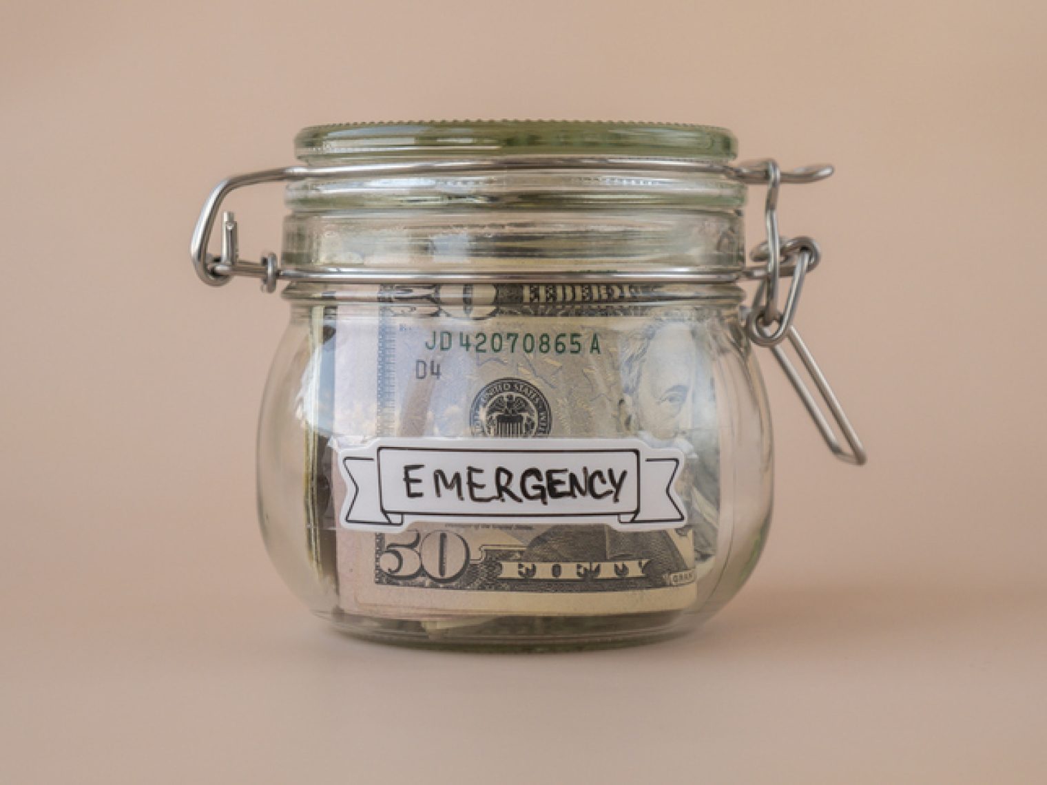 A glass jar with a secure lid labeled "EMERGENCY" contains a folded fifty-dollar bill, symbolizing savings for unexpected expenses.