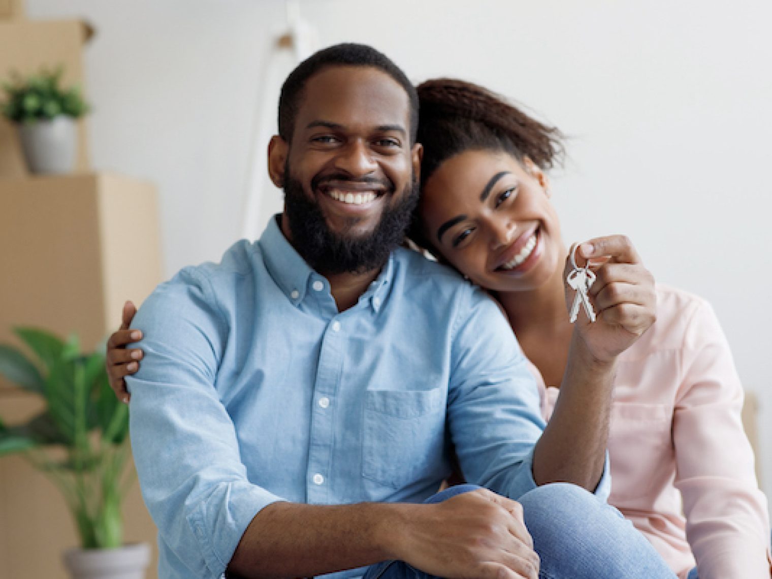 Glad cheerful young african american family show key and enjoy purchase of real estate in room with cardboard boxes.