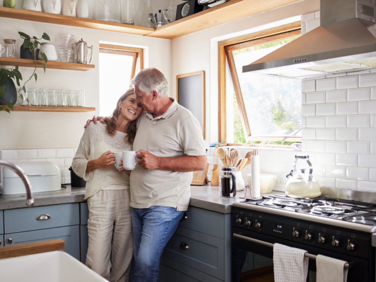 An affectionate couple shares a cozy moment in a well-lit kitchen with a cup of coffee, surrounded by modern appliances and decor.