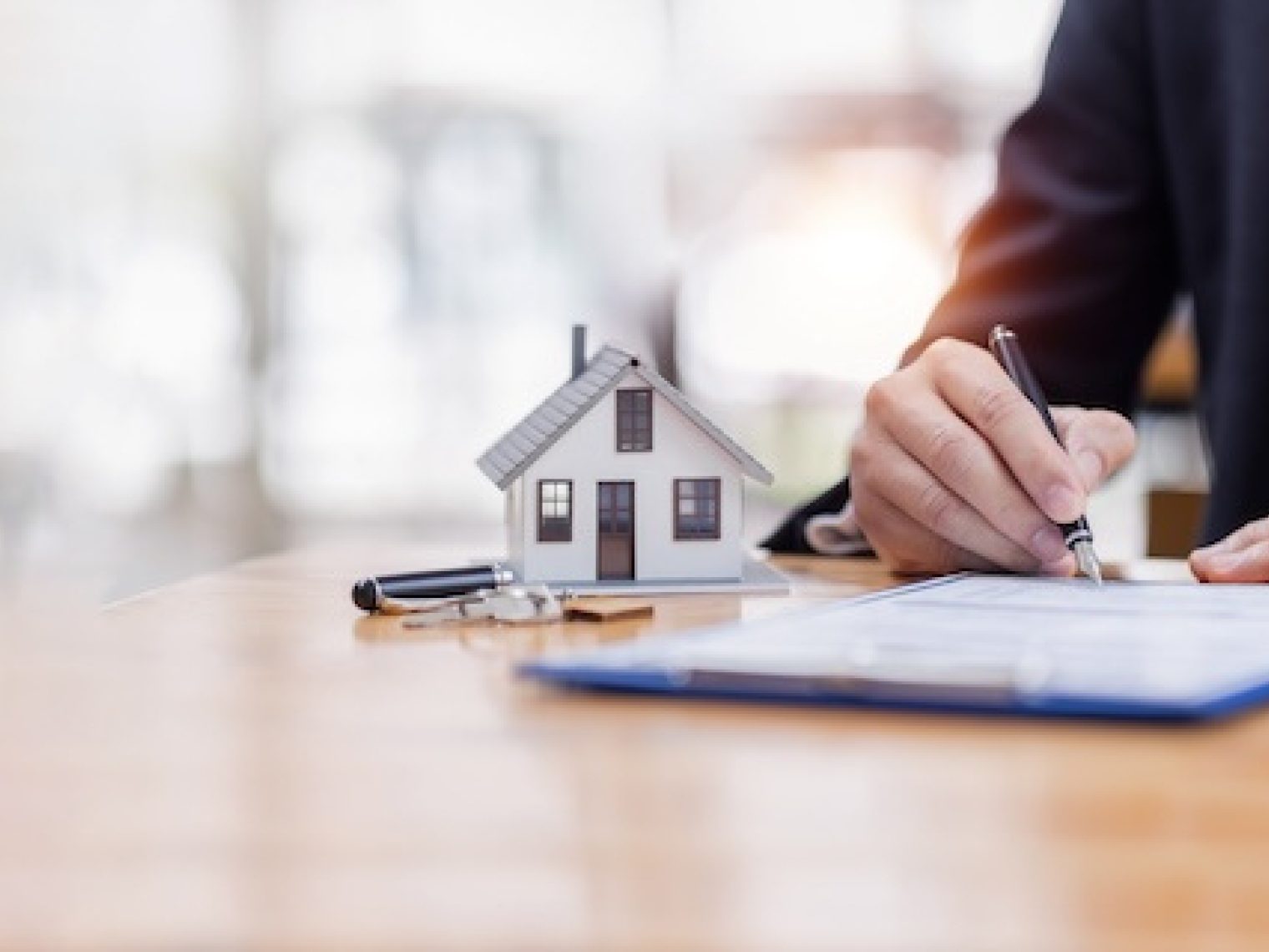 Man signs paper document next to model of a house.