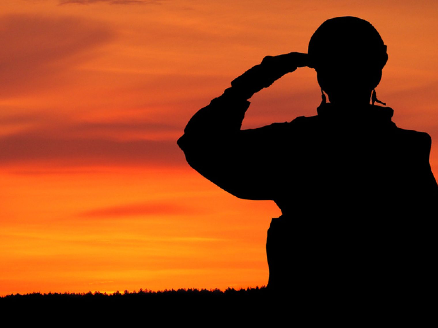 The silhouette of a soldier saluting against a vibrant sunset sky.