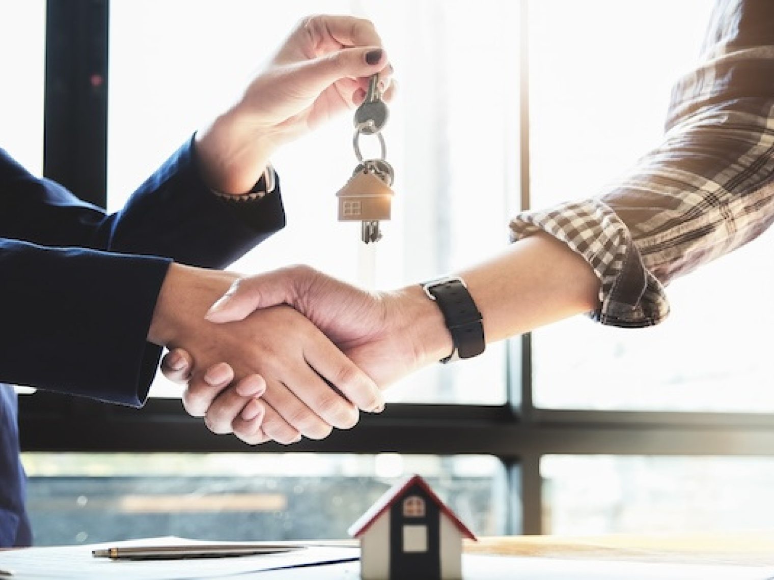 Real estate agent shakes homebuyer's hand while handing him house keys.