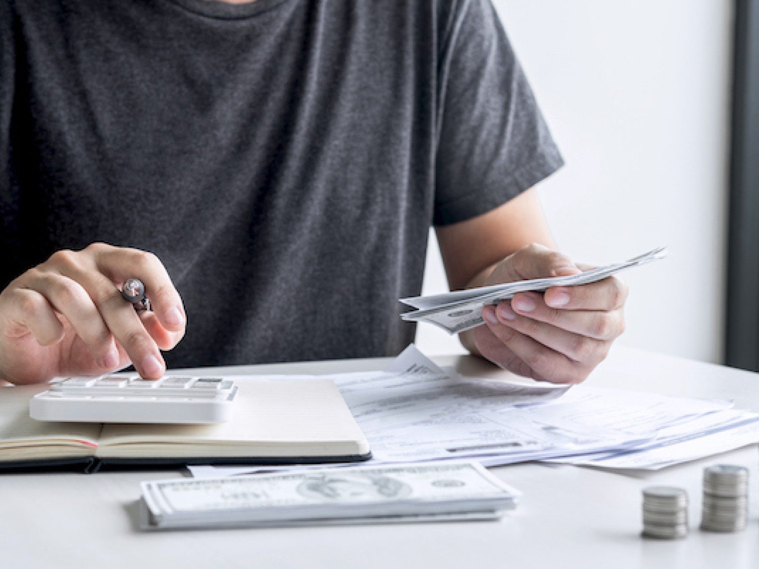 Slacked coin pile and man using calculator to calculating expenditure receipt bills of various activity cost and expenses.