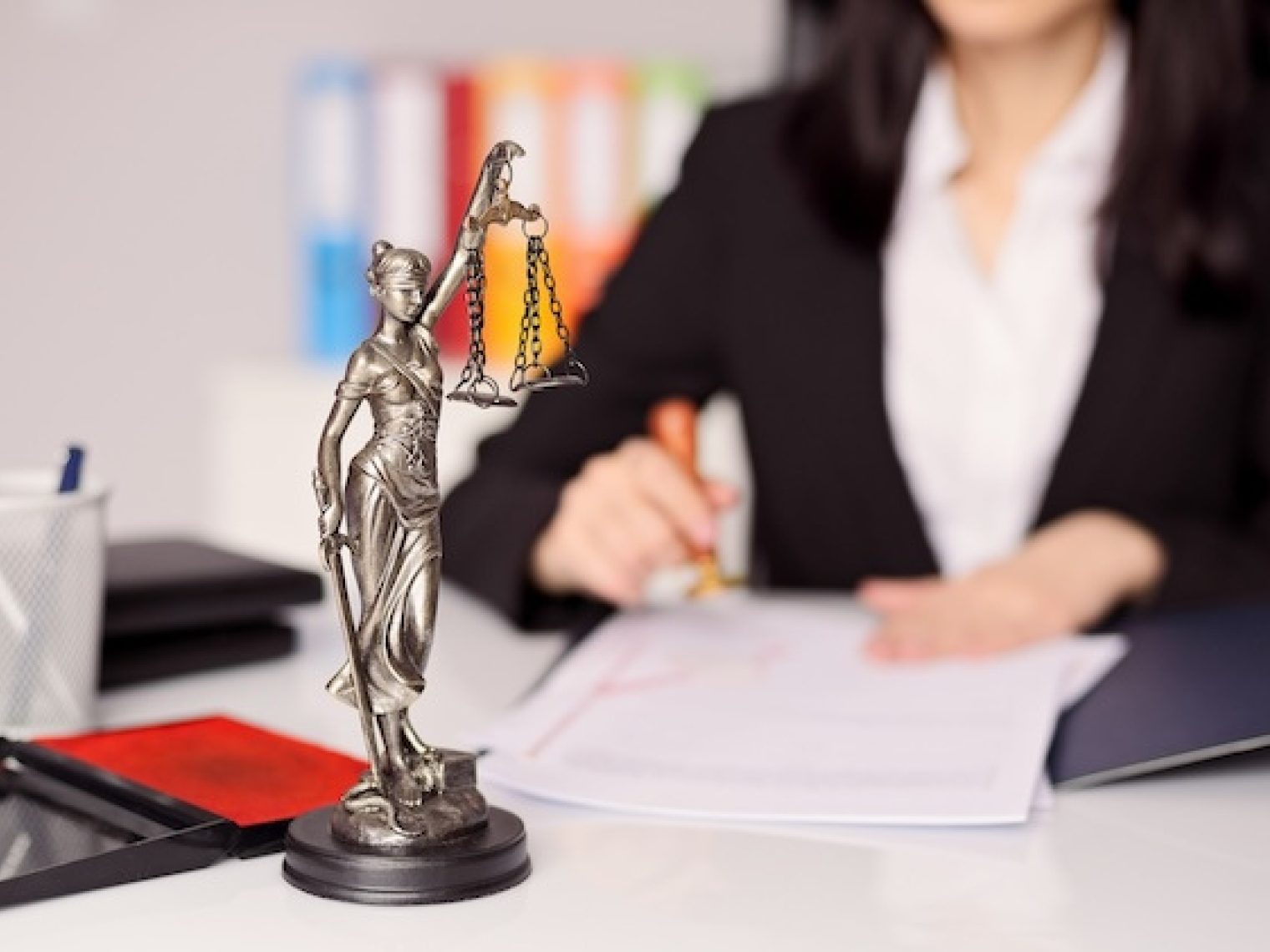 Small statue of goddess of justice on a lawyer's desk while she stamps a legal document.