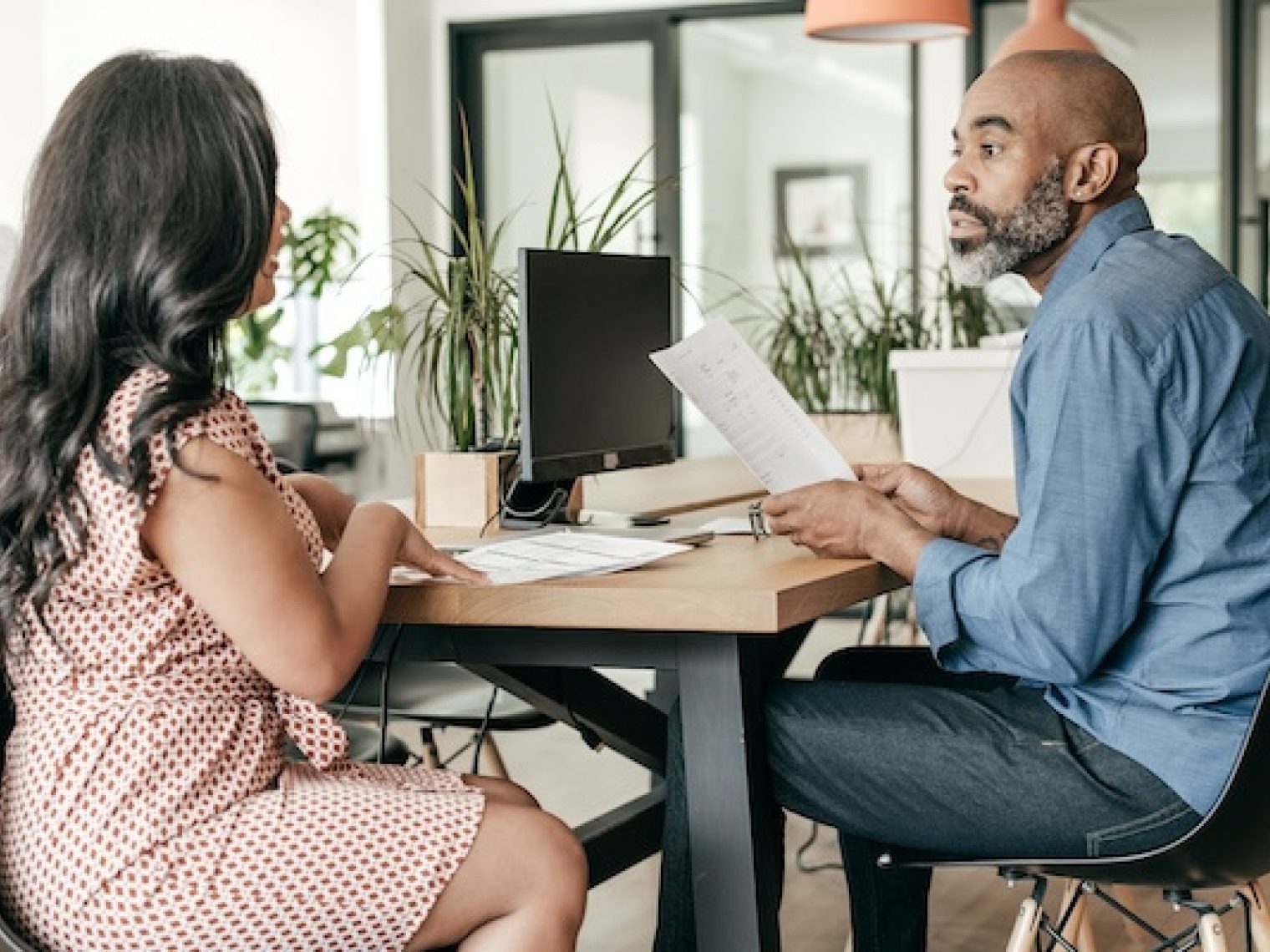 Man and woman sitting at table while discussing documents.