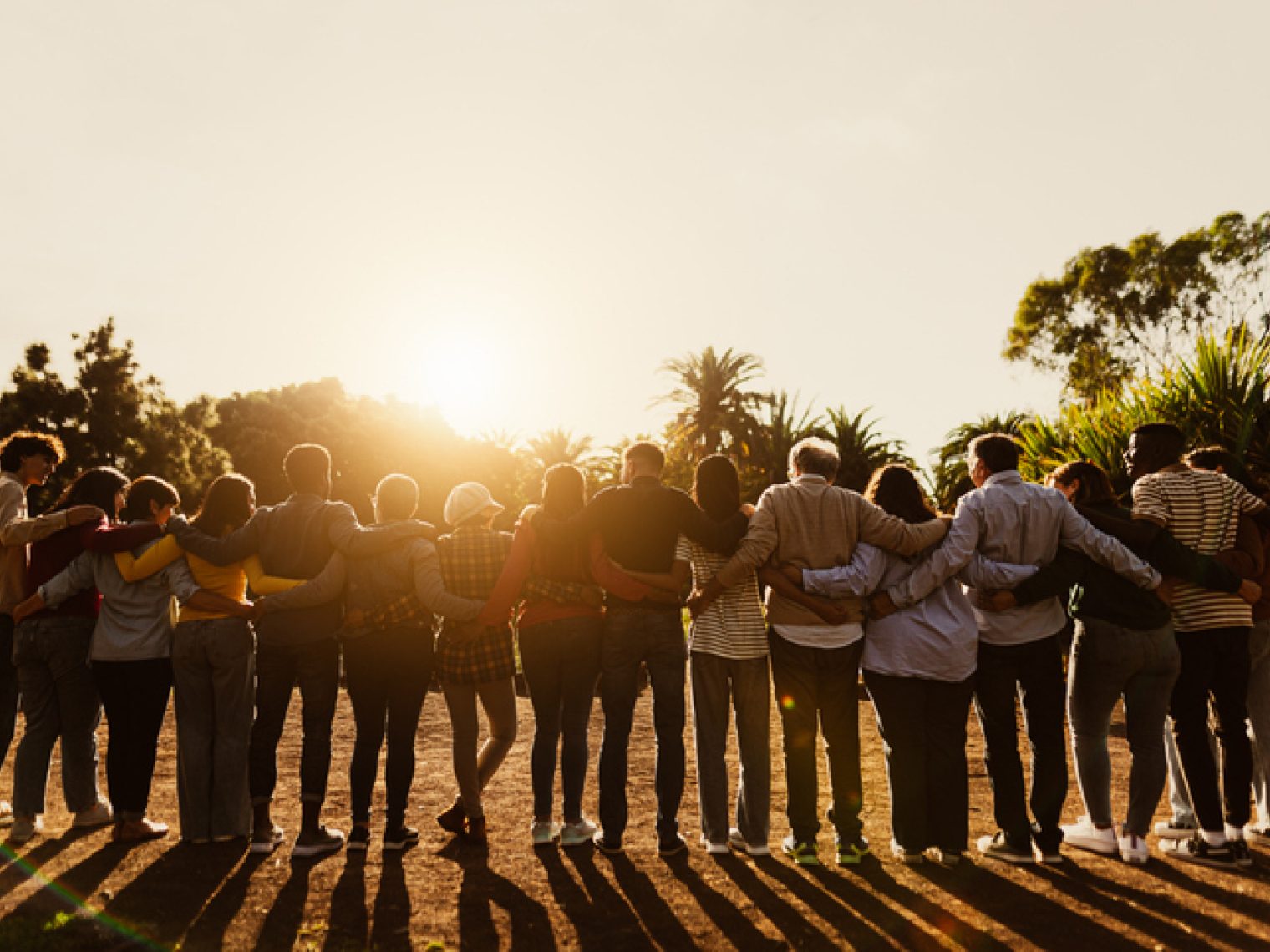 A group of people standing together with their arms around each other, looking towards the sunlight.