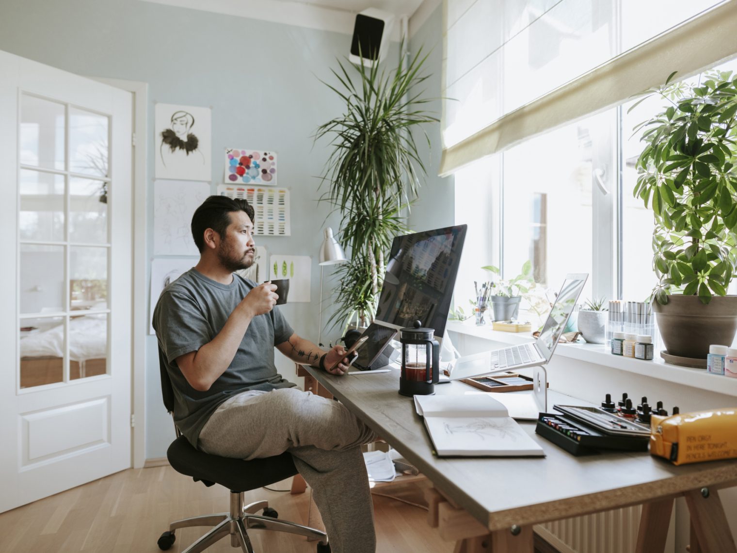 Man holding coffee in hand sitting at desk with a pensive look on his face.