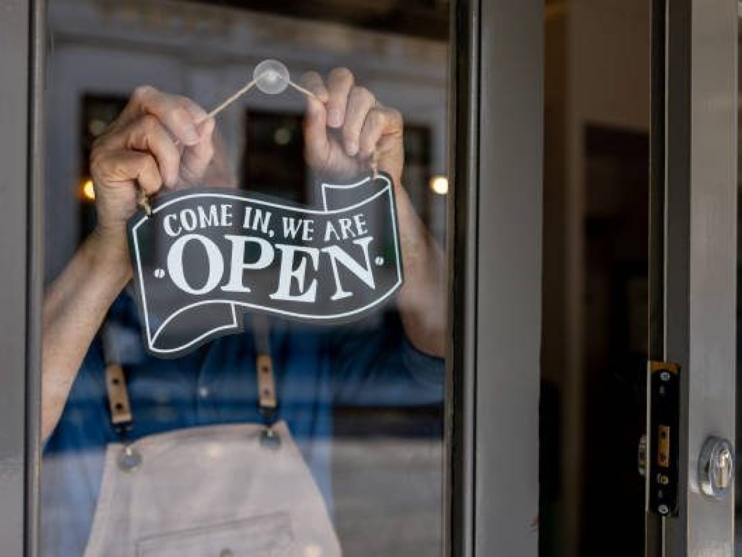 Hands Hang A Sign That Reads Come In, We Are Open On The Inside Of A Glass Door