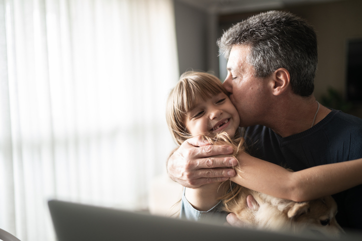 An affectionate moment of a father kissing his daughter on the cheek in their home.